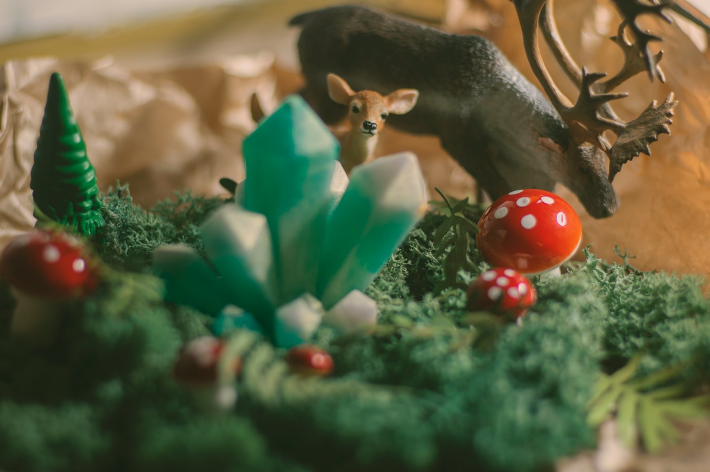 Toy deer and toadstools sit among moss and green crystals.