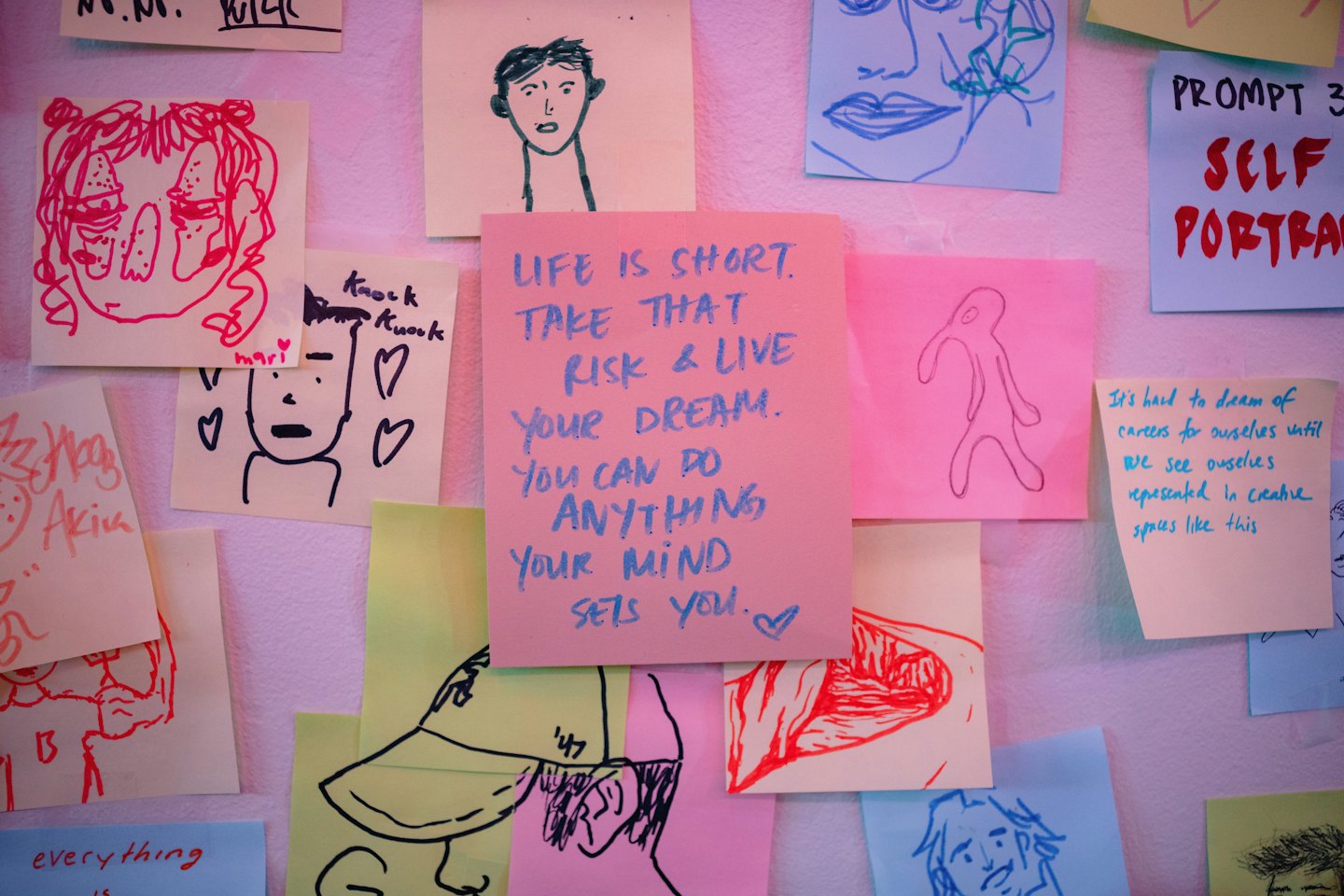 Sticky notes with hand-drawn faces cover a white wall.